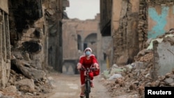 An Iraqi woman, dressed as Santa claus, rides her bicycle, amid the spread of the coronavirus disease (COVID-19), in the old city of Mosul, Iraq, December 18, 2020. Picture taken December 18, 2020. REUTERS/Abdullah Rashid 