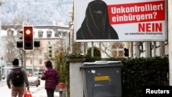 People walk past a poster of the Swiss Komitee gegen erleichterte Einbuergerung (Committee against an easier path to citizenship) seen on a display at the Hauptbahnhof central railway station in Zurich, Switzerland, Jan. 11, 2017. The poster reads, "Unchecked Naturalization? No to an easier path to citizenship." 