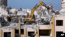 Palestinian workers use a backhoe to break and remove parts of the Al-Jawhara building, that was damaged in Israeli airstrikes during Israel's war with Gaza's Hamas rulers last May, in the central al-Rimal neighborhood of Gaza City, Nov. 16, 2021. (AP Photo/Adel Hana)