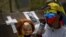 A protester with a Guy Fawkes mask, painted with the Venezuelan flag colors, carries a doll with a tear gas canister during a march in Caracas April 15, 2014.