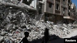 Children walk past the rubble of damaged buildings at Ain Tarma, and eastern Damascus suburb of Ghouta, Syria, July 19, 2017.