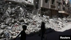 Anak-anak berjalan di antara puing-puing bangunan di Ain Tarma, distrik Ghouta, pinggiran Damaskus yang dikuasai pemberontak (foto: dok). Pasukan pro pemerintah meningkatkan serangan terhadap Ghouta timur. 