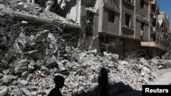 Des enfants marchent dans les ruines d'immeubles à Ain Tarma, dans la banlieue de Ghouta, Syrie, le 19 juillet 2017.