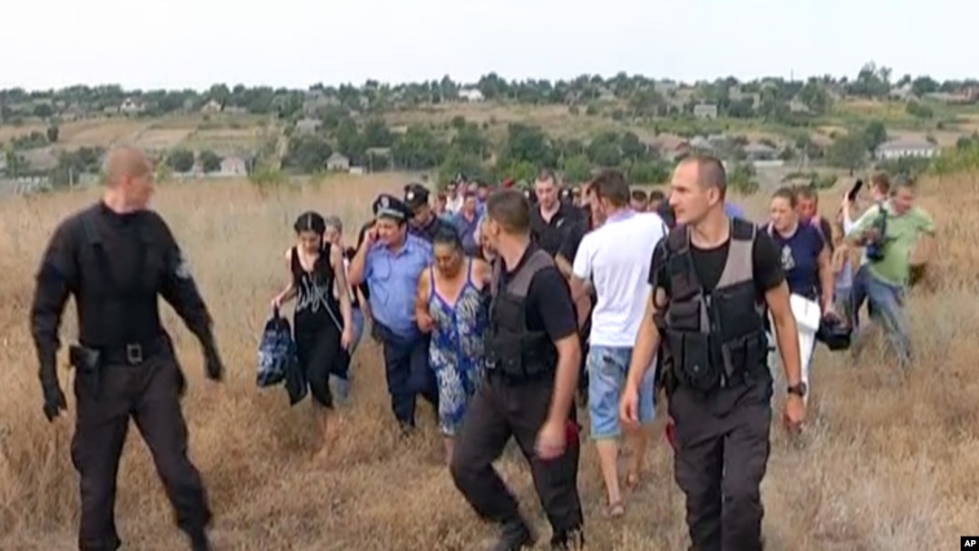 FILE - Ukrainian police officers escort the Roma residents from the village of Loshchynivka, Odessa region, Ukraine, in this image made from video taken Aug. 28, 2016. Ukrainian police evacuated a group of Roma residents from a southern town after villagers ransacked their homes.