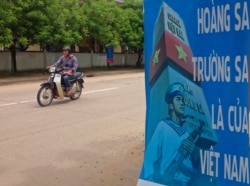 FILE - A man rides a motorcycle past a poster promoting Vietnam' sovereignty in the East Sea of the South China Sea, on Phu Quoc island, Sept. 11, 2014.