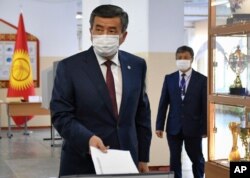 Kyrgyzstan's President Sooronbai Jeenbekov wearing a face mask casts his ballot paper during parliamentary elections in Bishkek, Kyrgyzstan, Sunday, Oct. 4, 2020.