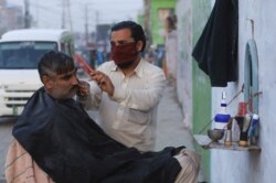 A barber wears a protective mask as a preventive measure amid coronavirus fears, as he gives a haircut to a customer along a road in Peshawar, Pakistan, March 13, 2020.