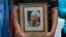 FILE - A man holds a tribute photograph as he watches the funeral service for former South African President Nelson Mandela on a large screen television in Cape Town, December 15, 2013.