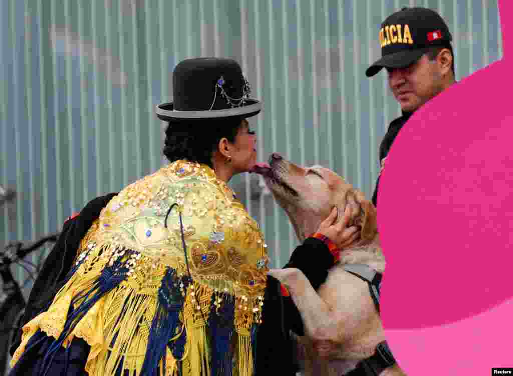 Peruvian dancer from the Andean city of Puno plays with a sniffer dog as a police officer stands guard outside the media center, ahead of the 2019 Pan American Games in Lima, Peru.