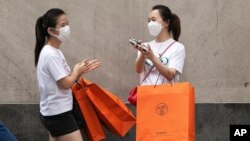 Women carrying Hermes shopping bags use hand sanitizer as they walk on Wall Street, July 30, 2020, in New York.