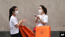 Women carrying Hermes shopping bags use hand sanitizer as they walk on Wall Street, July 30, 2020, in New York.