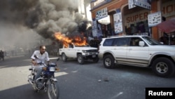 Un homme à moto passant à côté d'une voiture qui a été incendiée par des protestataires lors d'une manifestation contre le processus électoral à Port-au-Prince, en Haïti, le 18 janvier, 2016.