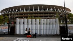 Des piétons portant des masques de protection, à la suite de l'épidémie de maladie à coronavirus (COVID-19), marchent devant le stade national, le stade principal des Jeux olympiques et paralympiques de Tokyo 2020 à Tokyo, Japon, le 7 juillet 2021.