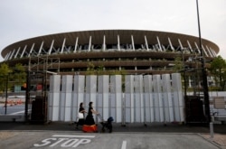 Pedestrians wearing protective masks, following the coronavirus disease (COVID-19) outbreak, walk in front of the National Stadium, the main stadium of Tokyo 2020 Olympics and Paralympics in Tokyo, Japan, July 7, 2021.