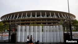 Pedestrians wearing protective masks, following the coronavirus disease (COVID-19) outbreak, walk in front of the National Stadium, the main stadium of Tokyo 2020 Olympics and Paralympics in Tokyo, Japan, July 7, 2021. 