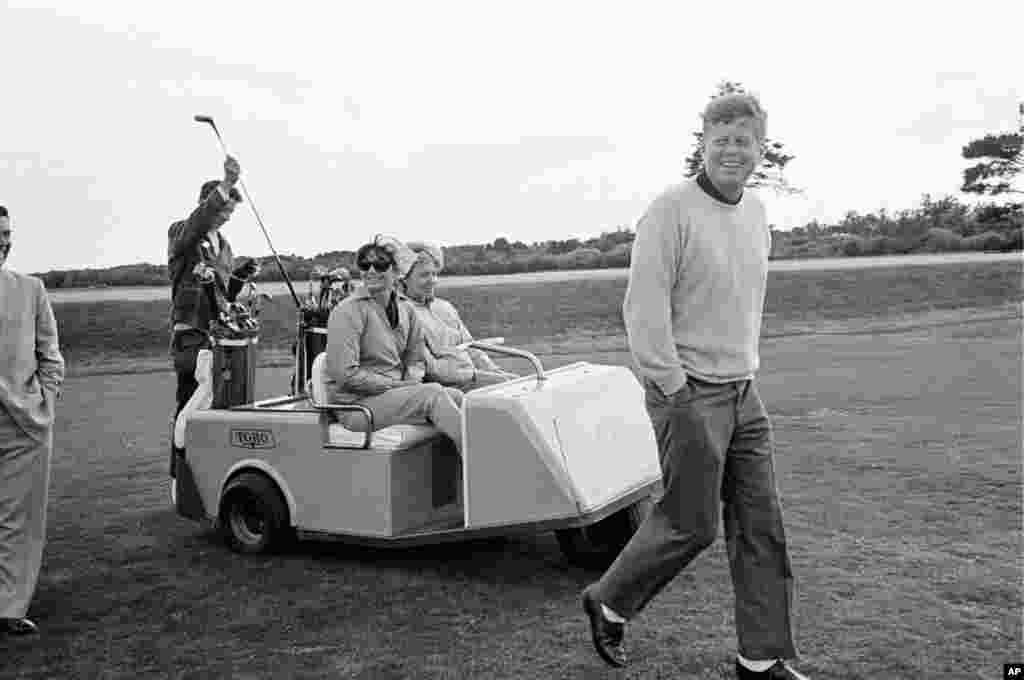 President Kennedy walks along the golf course after driving off from the tenth tee at the Country Club in Newport, Rhode Island, September 14, 1963. Mrs. Jacqueline Kennedy and Mrs.Tony Bradlee, wife of Washington Post senior editor Ben Bradlee, ride alon