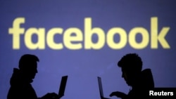 FILE - Silhouettes of laptop users are seen next to the Facebook logo in this picture illustration taken March 28, 2018. 