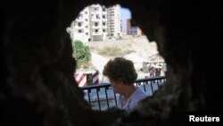 A woman is seen from a hole in her home's wall, caused by clashes between Sunni Muslims and Alawites in Tripoli, northern Lebanon, August 27, 2012. 