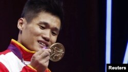 Lu Xiaojun mengamati medali emas yang diperolehnya untuk cabang angkat besi putra kelas 77 koligram di Olimpiade London 2012 (1/8). 