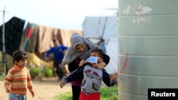 A Syrian refugee woman puts a face mask on a boy as a precaution against the spread of coronavirus, in al-Wazzani area, in southern Lebanon, March 14, 2020. 