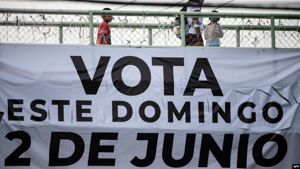 Una mujer y dos niños caminan sobre un puente peatonal del que cuelga una pancarta que llama a votar en las próximas elecciones generales en Xochimilco, México, el 31 de mayo de 2024.