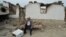A man sits in front of a destroyed house
