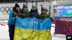 Ukraine's relay team, from left: Vita Semerenko, Juliya Dzhyma, Olena Pidhrushna and Valj Semerenko, with Ukrainian flag with writings on it after winning the gold in the women's biathlon 4x6k relay at the 2014 Winter Olympics, Feb. 21, 2014, in Krasnaya Polyana.