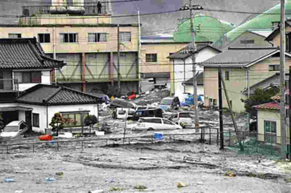 An earthquake-triggered tsunami washes away a warehouse and vehicles in Kesennuma, Miyagi prefecture (state), Mar 11 2011