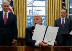 FILE - Then-Vice President Mike Pence, left, and then-White House Chief of Staff Reince Priebus watch as then-President Donald Trump displays an executive order to withdraw the U.S. from the 12-nation Trans-Pacific Partnership, Jan. 23, 2017.