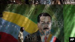 Un hombre con mascarilla pasa frente a un mural del presidente en disputa de Venezuela, Nicolás Maduro, en Caracas, Venezuela. Julio 22, 2020