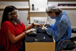 A beautician wearing protective gear tends to a customer wearing a protective face shield inside a parlor at a shopping mall in Ahmedabad, India, June 8, 2020.