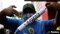 FILE - A man holds a mock syringe as demonstrators protest against Sao Paulo state governor Joao Doria and China's Sinovac COVID-19 vaccine, in Sao Paulo, Brazil, Nov. 1, 2020.