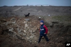 ARHIVA - Dečak stoji kod kratera nastalog posle eksplozije u selu Čermalik na istoku Ukrajine, 26. februara 2015.