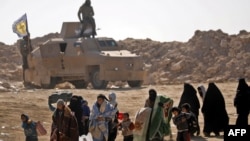 Civilians fleeing the battered Islamic State-held holdout of Baghuz walk past an armored vehicle belonging to the Manbij military council into a nearby area held by the Syrian Democratic Forces (SDF) in Syria, Feb. 12, 2019.