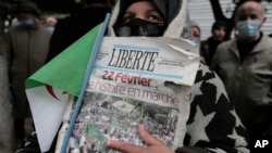 FILE - A woman holds a newspaper headlining "Feb.22, History coming" as Algerians demonstrate in Algiers to mark the second anniversary of the Hirak movement, Monday Feb. 22, 2021.