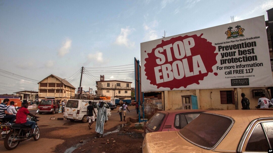 FILE - People pass a banner reading "STOP EBOLA" forming part of Sierra Leone's Ebola-free campaign in Freetown, Jan. 15, 2016.