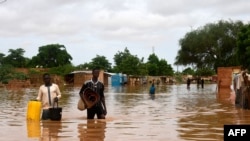 People, carrying their belongings, walk down a flooded street in the Kirkissoye neighborhood in Niamey, Niger, Aug. 27, 2020.