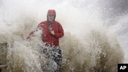 A news reporter standing near a sea wall in Cedar Key, Fla., is covered by an unexpected wave as Hurricane Hermine nears the Florida coast, Sept. 1, 2016. 