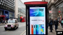 FILE - Pedestrians walk past a Huawei ad at a bus stop in central London, April 29, 2019.