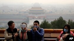 FILE - Visitors, some wearing masks to protect themselves from pollutants, share a light moment as they take a selfie at the Jingshan Park on a polluted day in Beijing, Monday, Dec. 7, 2015.