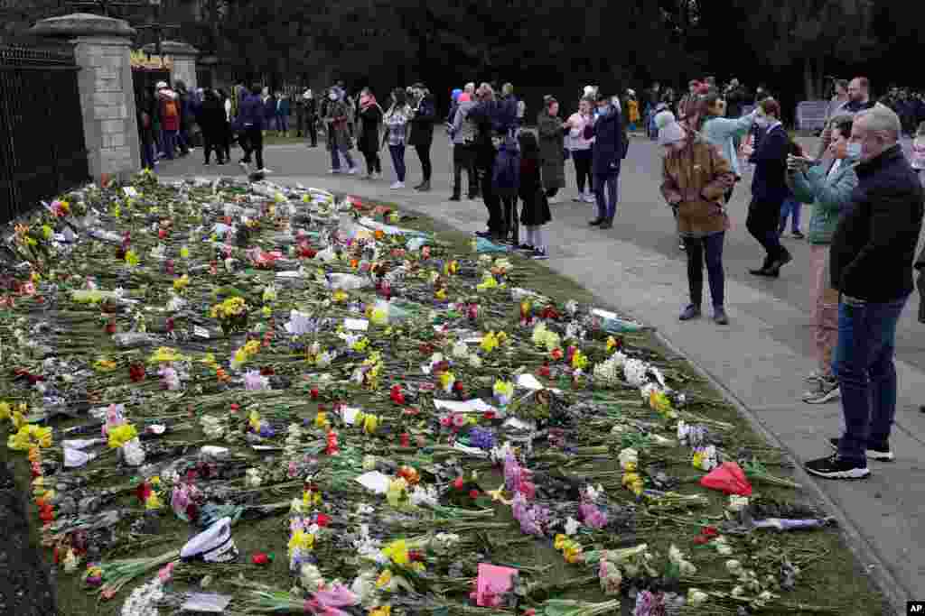 People look at flowers outside Windsor Castle in Windsor, England, to pay tribute to Britain's Prince Philip, the irascible and tough-minded husband of Queen Elizabeth II. 