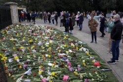 People look at flowers outside Windsor Castle in Windsor, England, to pay tribute to Britain's Prince Philip, the irascible and tough-minded husband of Queen Elizabeth II.