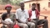 Silas Bihizi, center, sits with Valens Rukiriza, right, Rukiriza's wife and one of their grandchildren outside the Rukiriza family home in Buguli, Rwanda. 