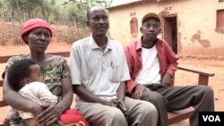 Silas Bihizi, center, sits with Valens Rukiriza, right, Rukiriza's wife and one of their grandchildren outside the Rukiriza family home in Buguli, Rwanda. 