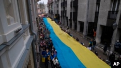 Ljudi nose ogromnu ukrajinsku zastavu kako bi obilježili prvu godišnjicu ruske invazije na Ukrajinu u Viljnusu, Litvanija, u petak, 24. februara 2023. (AP Photo/Mindaugas Kulbis)