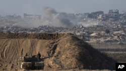 Un soldat israélien regarde une partie détruite de la ville de Gaza tandis que d'autres se tiennent sur un véhicule blindé à la frontière entre Israël et Gaza, vue du sud d'Israël, le 1er décembre 2024. (AP Photo/Tsafrir Abayov)