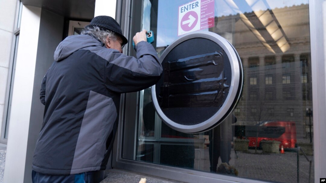 A person looks through the glass as the sign of the U.S. Agency for International Development, or USAID, is seen taped over at the agency headquarters in Washington, Feb. 7, 2025.