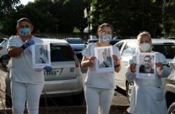 FILE - Health professionals hold up photos of people they say were their colleagues who died of COVID-19, as they protest outside "Pronto Socorro 28 de Agosto" Hospital, in Manaus, Brazil, April 27, 2020.