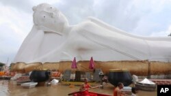 Buddhist monks paddle a boat through floodwaters in front of a reclining Buddha at the Wat Satue in Ayutthaya province north of Bangkok.