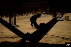 An Indigenous Juma youth holds a baby in a hammock in her community, near Canutama, Amazonas state, Brazil, Sunday, July 9, 2023. (AP Photo/Andre Penner)